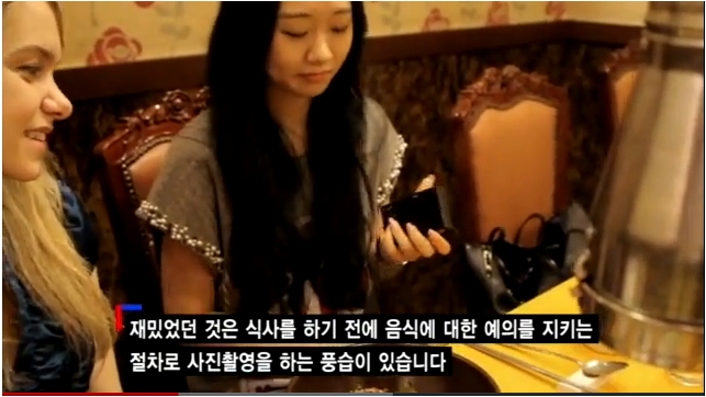 영상 장면: 한국 식당의 모습과 함께 외국인이 식사를 준비하는 모습. 자막: "재밌었던 것은 식사를 하기 전에 음식에 대한 예의를 지키는 절차로 사진촬영을 하는 풍습이 있습니다."